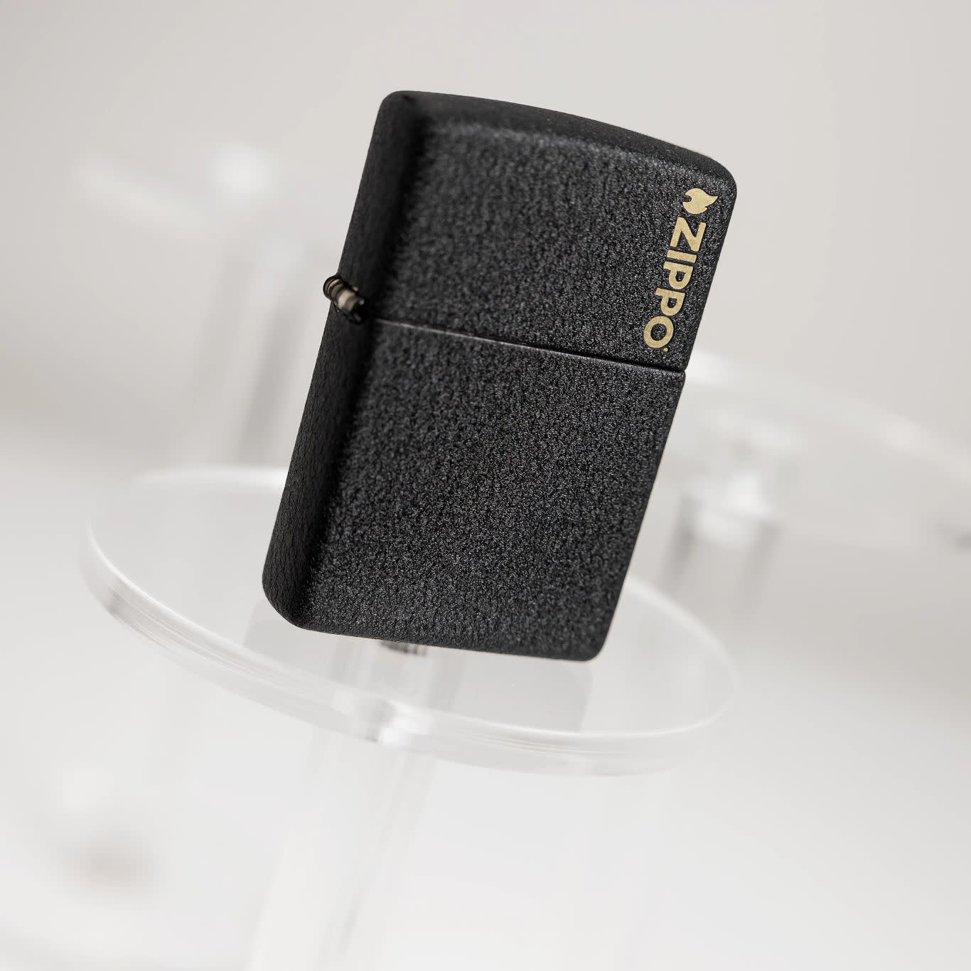 Lifestyle image of Zippo Classic Black CrackleÂ® Zippo Logo Windproof Lighter standing on a clear pedestal with the image at an angle.
